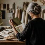 Una professionista della moda osserva campioni di tessuto e bozzetti sul tavolo di un atelier.